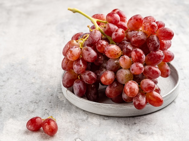 Um cacho de uvas vermelhas maduras com as gotas de água na placa de cerâmica cinza