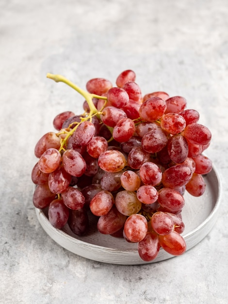 Um cacho de uvas vermelhas maduras com as gotas de água na placa de cerâmica cinza