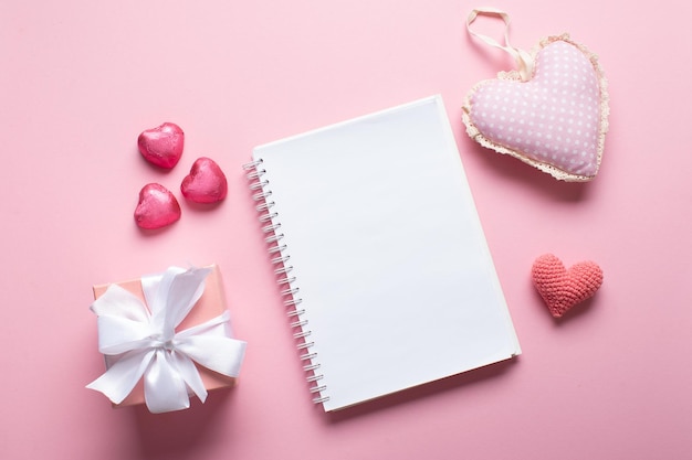 Foto um caderno aberto com um presente e doces em um fundo rosa claro dia dos namorados