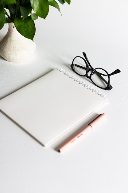 Um caderno branco com uma caneta rosa e óculos pretos está sobre um fundo branco