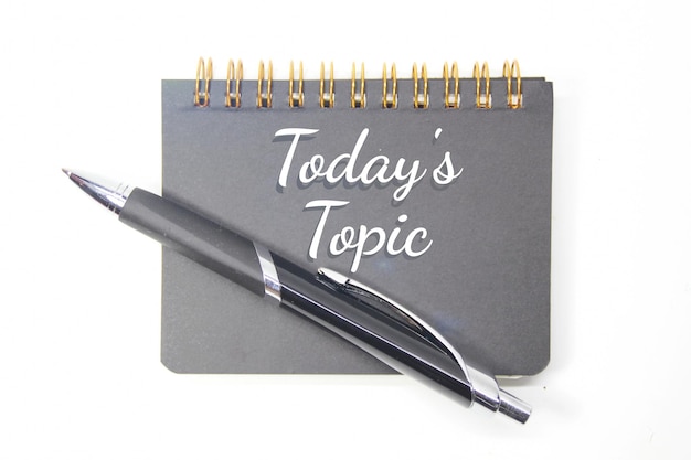 Um caderno cinza com uma caneta e uma caneta que diz o assunto de hoje.