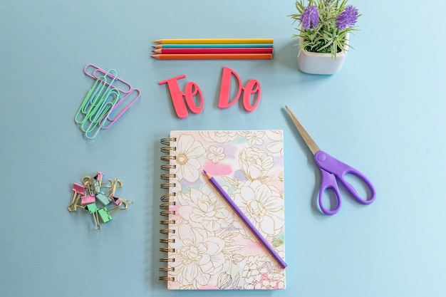 Foto um caderno com um bloco de notas rosa para fazer e uma caneta em uma mesa azul.