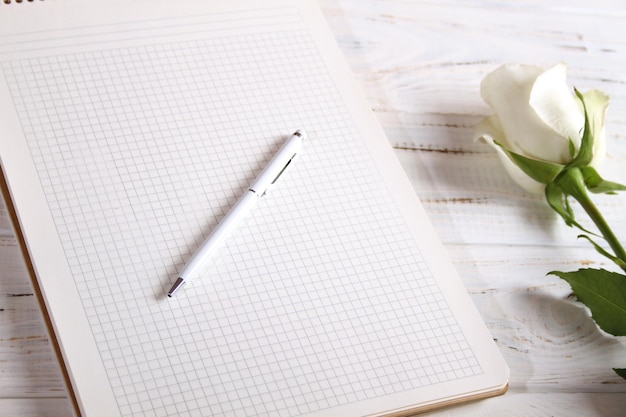 Um caderno grande com uma caneta branca e uma linda rosa branca