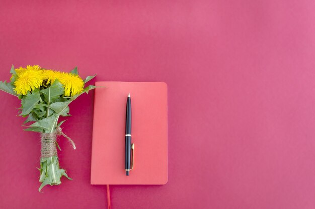 Foto um caderno vermelho uma caneta e um buquê de flores amarelas