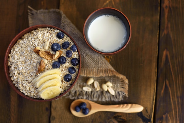 Foto um café da manhã saudável em madeira escura: aveia, leite, nozes e mirtilos. vista do topo