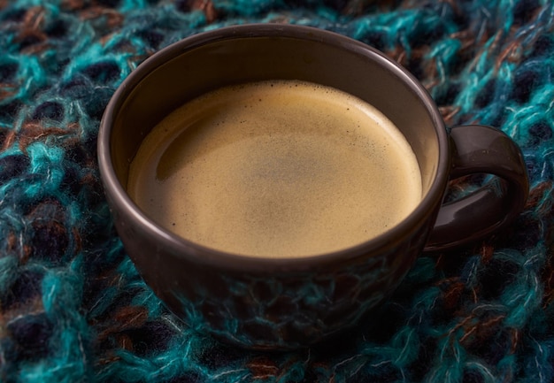 Um café expresso fresco em uma xícara escura no fundo do cachecol de lã quente