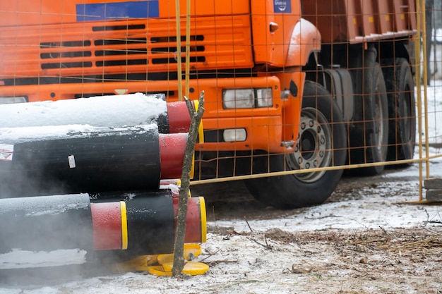 Um caminhão basculante com um táxi vermelho fica em um canteiro de obras no inverno perto de novos canos de água Um caminhão basculante para transporte de solo