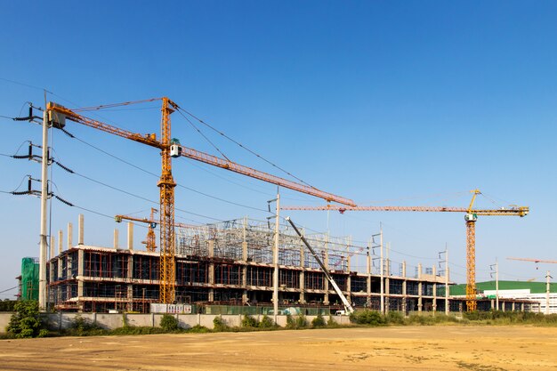 Um canteiro de obras, incluindo vários guindastes trabalhando em um prédio, Boom crane na construção de um arranha-céus e andaimes no prédio, com céu azul