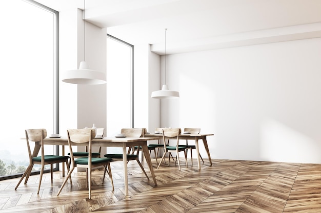 Um canto de café branco moderno com um chão de madeira e mesas quadradas com cadeiras verdes perto delas. Grandes janelas e uma parede em branco.