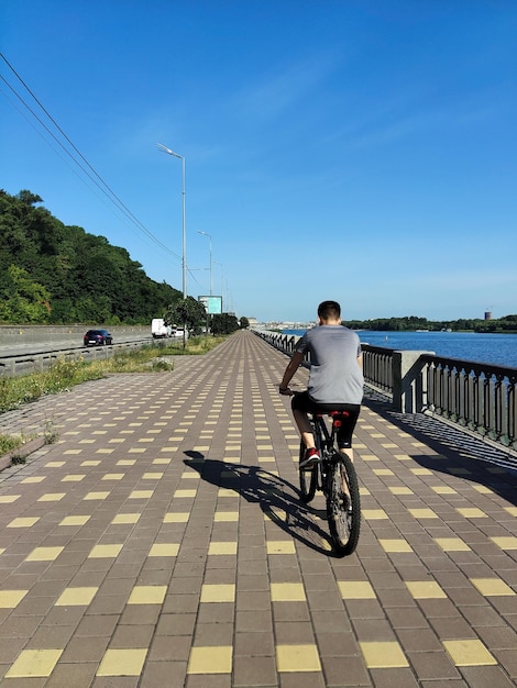 Um cara anda de bicicleta em um caminho reto em perspectiva perto de um rio Vista traseira