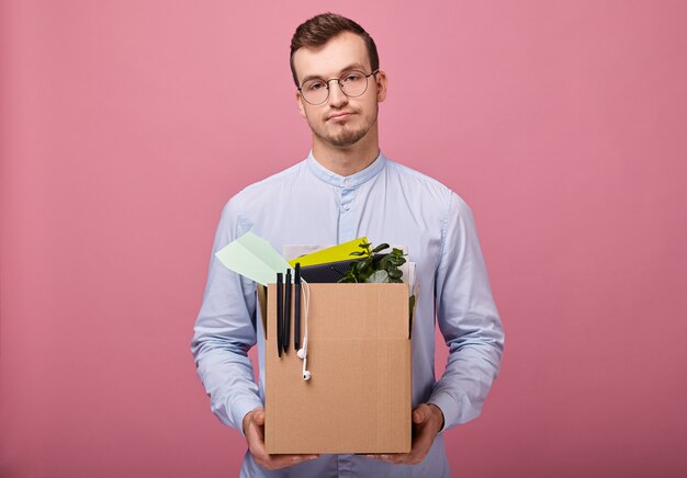 Um cara bonito e legal em uma camisa azul celeste está com uma caixa de papelão nas mãos