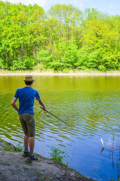 Um cara com um chapéu leve está pescando em um rio pitoresco no verão