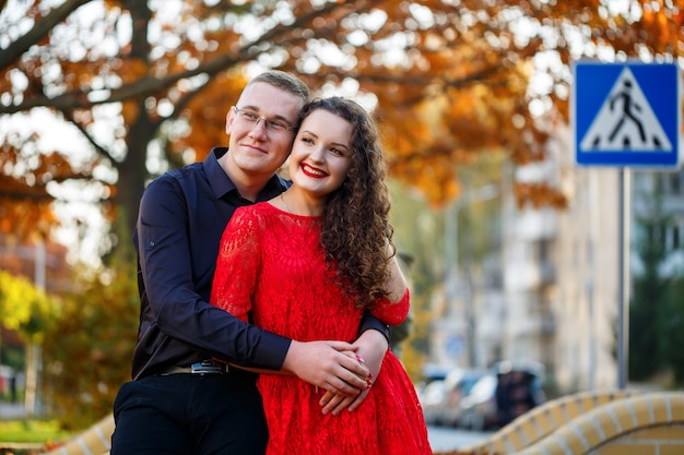 Um cara com uma camisa preta e uma garota com cachos em um vestido vermelho em um beco no outono