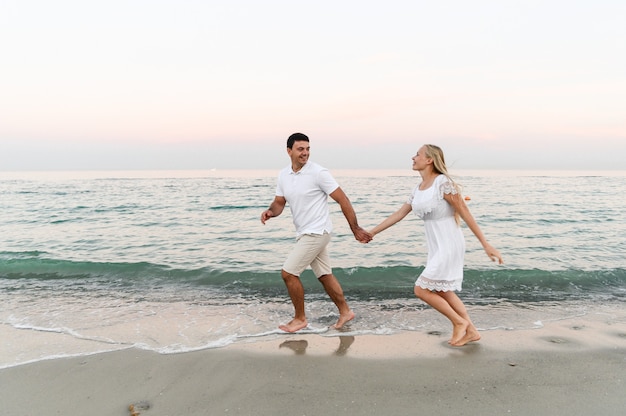 Um cara com uma garota com roupas de verão está caminhando à beira-mar. marido e mulher em um romântico pôr do sol do dia, perto do mar. os amantes correm ao longo da praia.