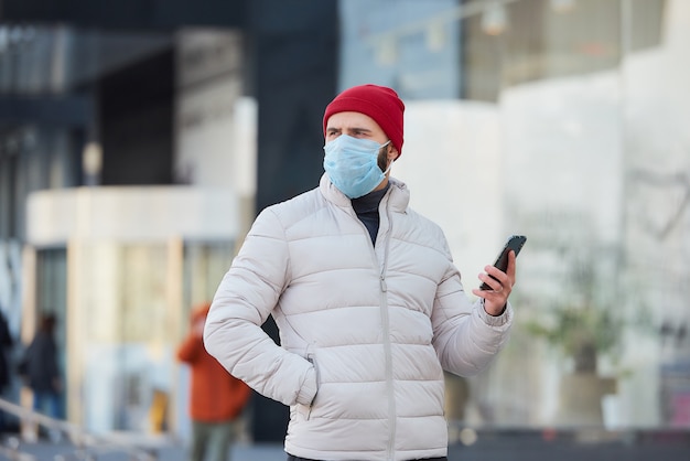 Um cara com uma máscara no rosto usando um smartphone no centro da cidade.