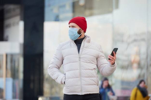 Um cara com uma máscara no rosto usando um smartphone no centro da cidade.