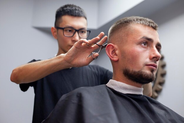 Um cara corta o cabelo em uma barbearia, um jovem barbeiro cazaque corta manualmente com uma tesoura