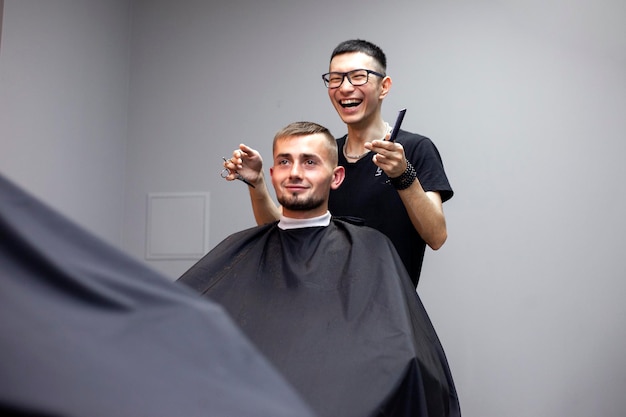 Um cara corta o cabelo em uma barbearia, um jovem barbeiro cazaque corta manualmente com uma tesoura