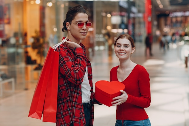 Um cara dá a sua namorada uma caixa em forma de coração no Dia dos Namorados. Jovem casal em shopping.