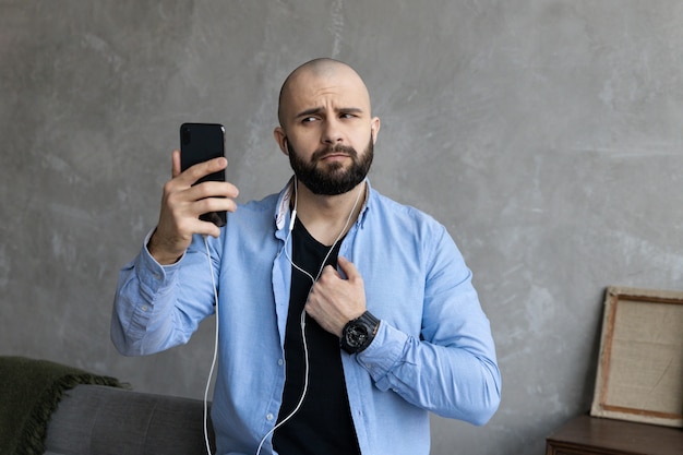 Um cara de camisa azul e calça jeans preta está ao telefone em um link de vídeo em casa. O conceito de trabalho freelance