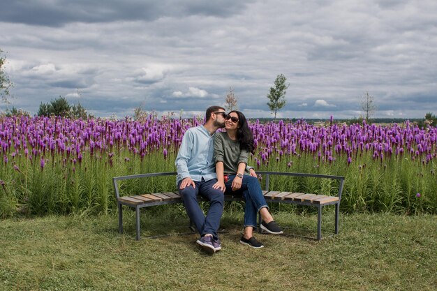 Um cara e uma garota apaixonada estão sentados em um banco no parque perto de flores