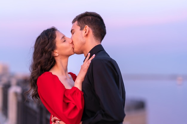 um cara e uma garota se beijam ao pôr do sol na margem perto do rio