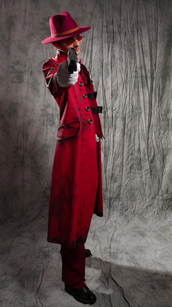 Um cara elegante em uma fantasia de vampiro um chapéu vermelho um casaco e óculos escuros apontando uma arma