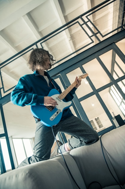 Um cara louco de cabelos compridos. Posando cara bonito com corte de cabelo ondulado profissionalmente tocando guitarra e se sentindo uma estrela do rock