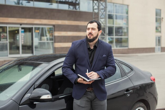 Um cara moreno com barba perto de um carro preto