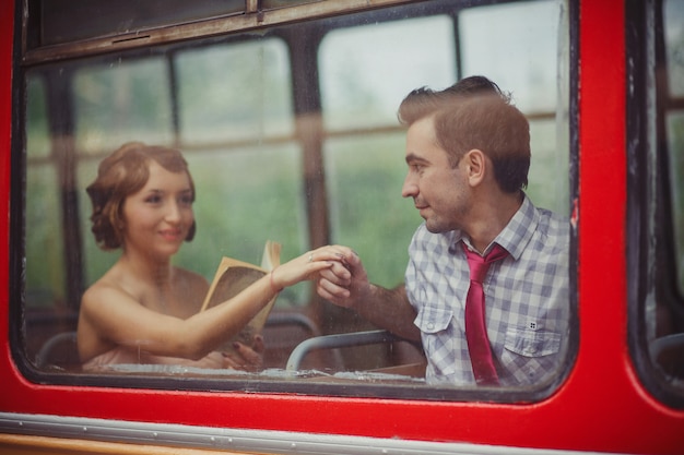 Um cara segura a mão de uma garota que está lendo um livro. Viagem de ônibus