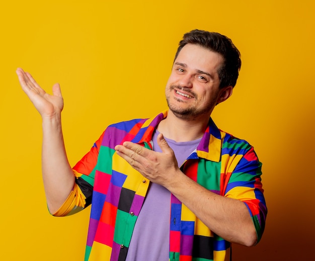 Foto um cara sorridente com uma camisa dos anos 90 aponta com as mãos