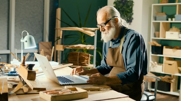 Um carpinteiro focado desenvolve layouts de modelos de madeira d esboços usando um laptop