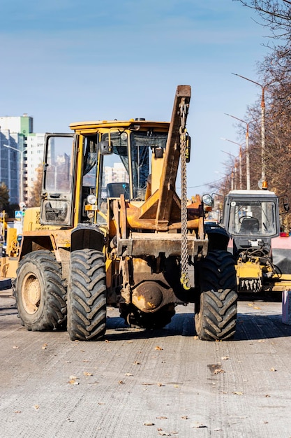 Um carregador frontal pesado transporta a terra em uma caçamba e inclina a estrada. reparação de estradas no centro de uma cidade moderna no outono. maquinaria de construção pesada para movimentação de solo.