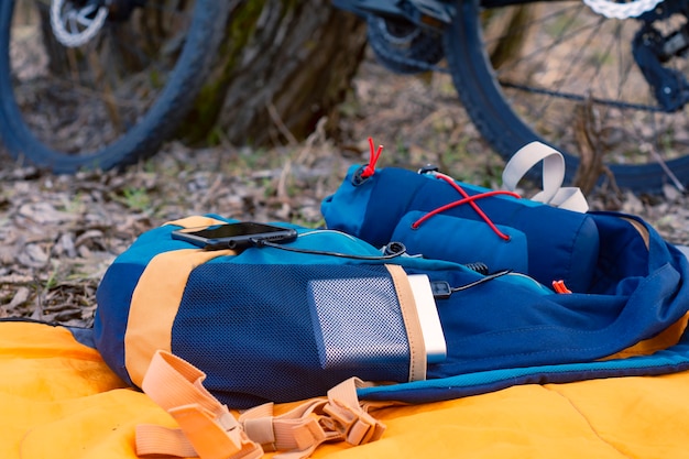 Um carregador portátil carrega o smartphone. banco de potência com cabo no contexto de madeira e bicicleta.