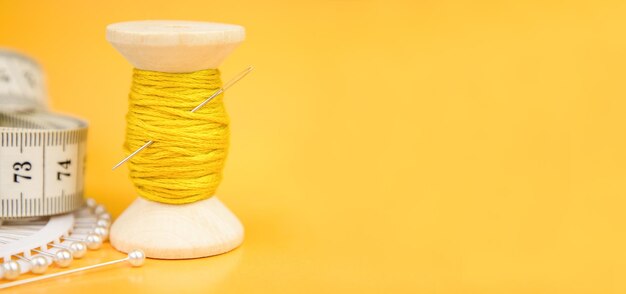 Foto um carretel de linha amarela uma agulha e um dedal em um fundo amarelo