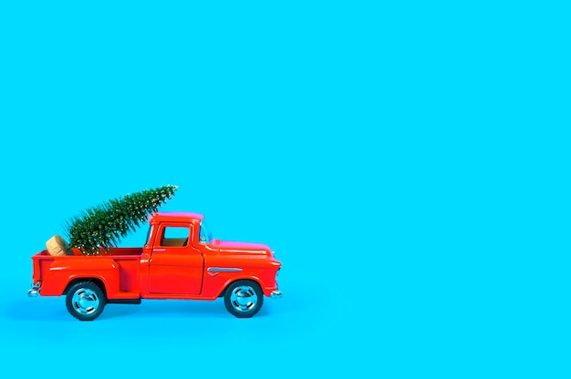 Um carro antigo vermelho carrega uma árvore de Natal verde sobre um fundo azul na parte de trás.