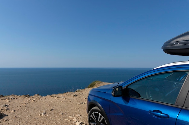 Um carro azul com um rack de teto na beira de um penhasco contra o céu azul e o mar Conceito de viagem de carro Foto de alta qualidade