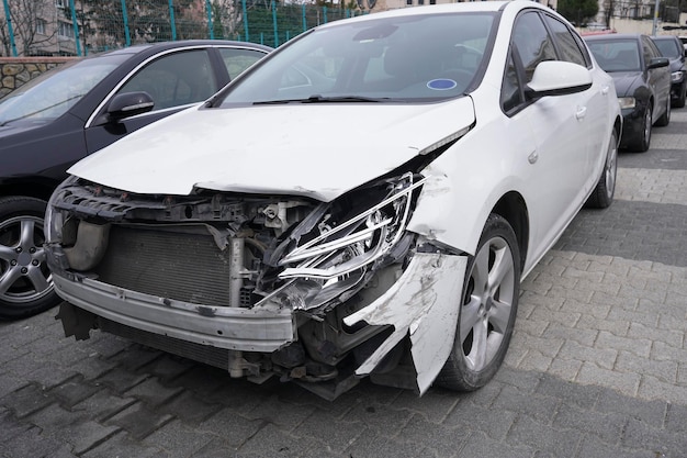 Um carro branco estacionado na rua com faróis quebrados.