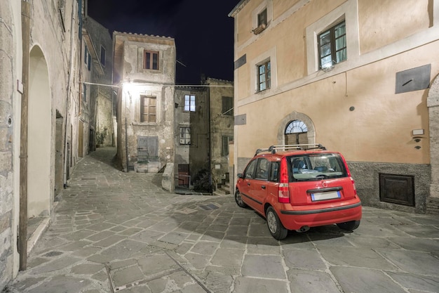 Um carro vermelho italiano típico em uma rua estreita em uma cidade velha italiana à noite Sorano Toscana Itália