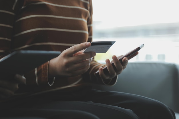 Foto um cartão de crédito nas mãos de uma jovem empresária paga um negócio em um celular e em uma mesa com um laptop