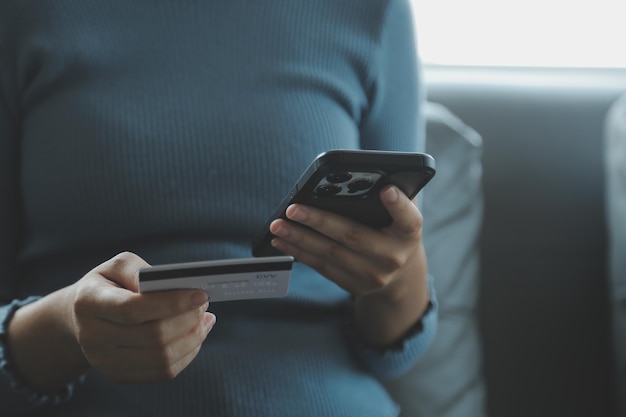 Um cartão de crédito nas mãos de uma jovem empresária paga um negócio em um celular e em uma mesa com um laptop