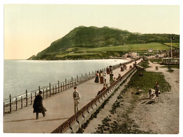 um cartão postal de pessoas caminhando ao longo de uma praia com uma montanha no fundo