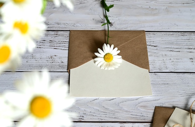 Um cartão vazio com um envelope marrom e uma flor branca para a mãe em uma mesa de madeira em estilo vintage e com vinhetas