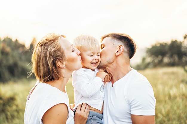 Um casal a beijar um filho bonito no campo contra um céu claro.