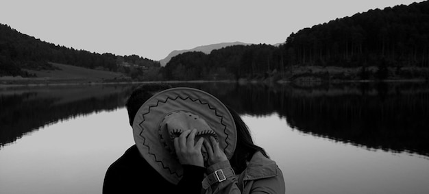 Foto um casal a namorar atrás de um chapéu contra o lago e as montanhas.