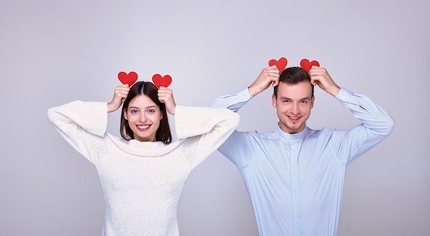 Um casal adorável de amantes com um humor brincalhão no dia de São Valentim mantém dois corações vermelhos de papelão