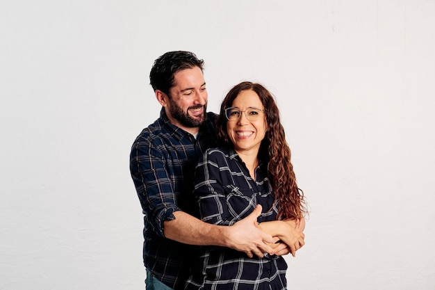 Foto um casal adulto caucasiano em camisas xadrez em pé e mostrando os polegares para a câmera e sorrindo contra um fundo branco.