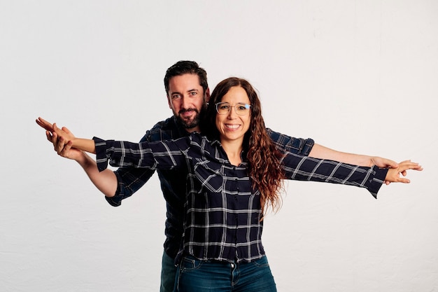 Foto um casal adulto caucasiano em camisas xadrez em pé e mostrando os polegares para a câmera e sorrindo contra um fundo branco.