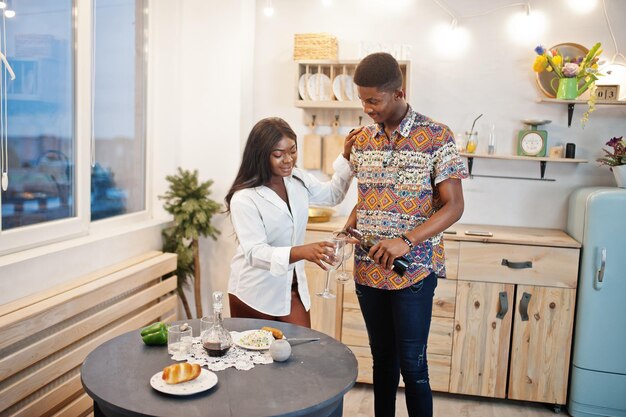 Um casal afro-americano a beber vinho na cozinha no seu encontro romântico.