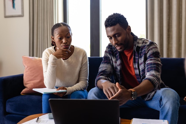 Um casal afro-americano a fazer papelada usando um portátil em casa. Estilo de vida, relacionamento, convivência, comunicação e vida doméstica, inalterados.